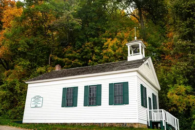 A white historic schoolhouse surrounded by colorful autumn foliage in Taylors Falls, Minnesota.